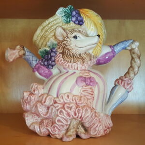 Hand-painted ceramic teapot featuring the Big Bad Wolf from Little Red Riding Hood dressed as Grandma. The teapot is styled in a frilly pink-and-cream Victorian dress with a bonnet adorned with grapes and bows. Spout and handle are formed from her gloved arms. Glossy glaze finish and theatrical expression give it a storybook feel.