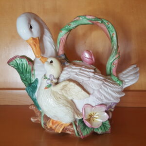 Hand-painted ceramic teapot by Fitz and Floyd featuring a mother duck and duckling nuzzling affectionately, surrounded by pastel flowers and leaves. The handle is shaped like a green and pink flowering vine. The teapot has a glossy finish and detailed feather textures.