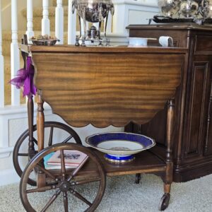 Vintage 1940s Colonial Revival tea cart with glass top, drop-leaf sides, and wooden spoke wheels. Front close up