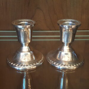 Pair of vintage Duchin Creation sterling silver weighted candlestick holders with flared bases and beaded rims, displayed on a glass shelf with a warm wood background. Light tarnish and patina visible on polished surfaces.