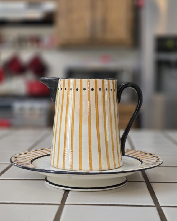 A hand-painted Atelier Primavera pitcher and matching plate with Art Deco stripes and polka dots, showing visible crazing and a chipped edge.